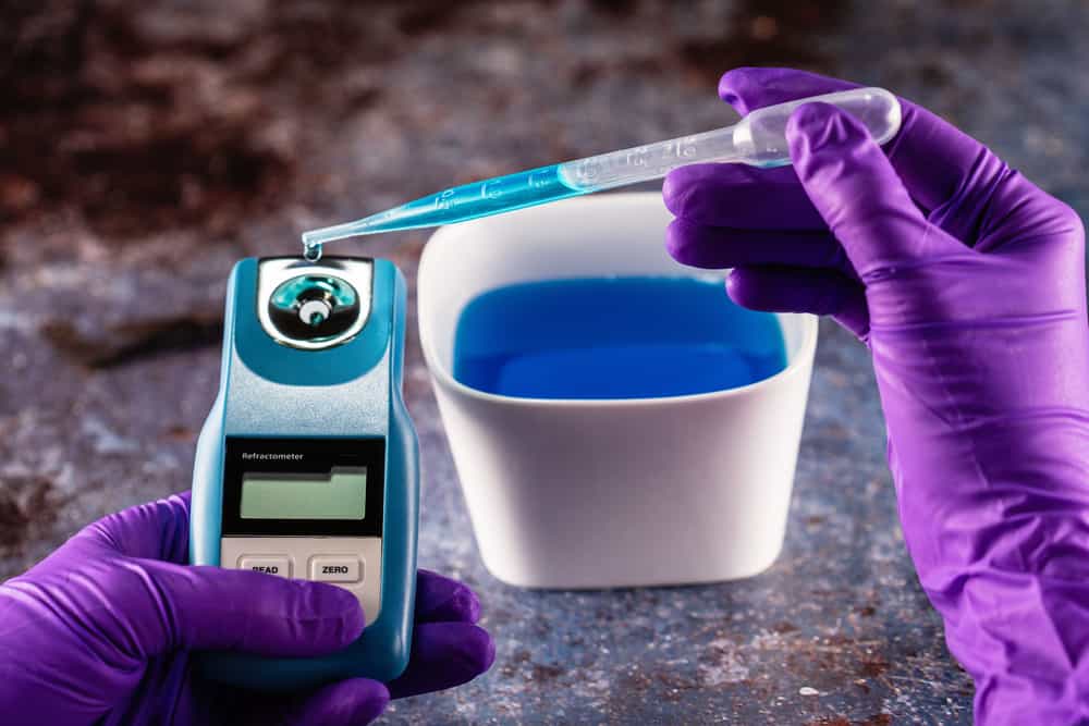Hands wearing purple medical gloves placing liquid sample on digital refractometer
