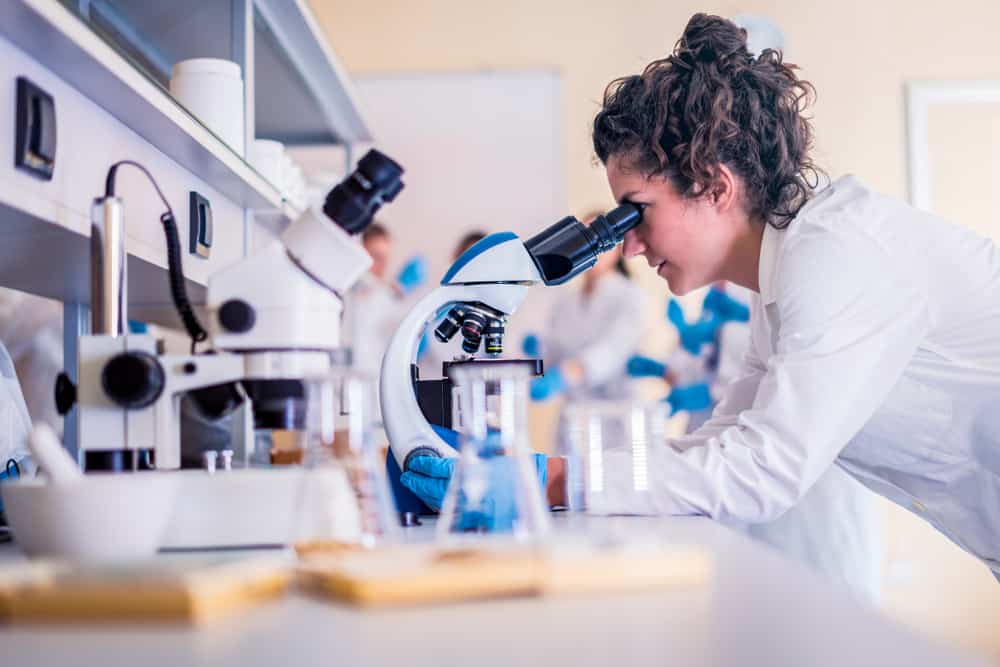 Young-female-scientist-in-lab-coat-looking-in-microscope-in-lab-setting