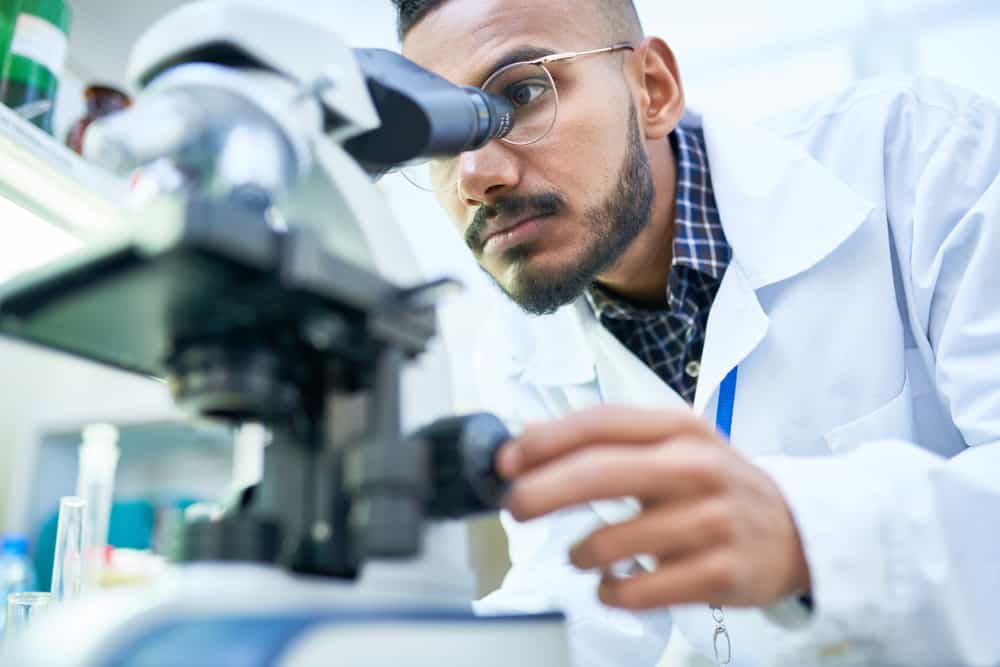 Young-multiracial-male-scientist-with-glasses-looking-into-microscope