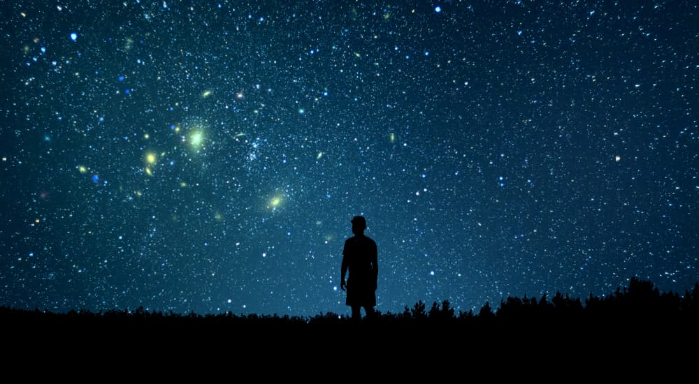 Silhouette of man standing alone staring up at star-filled sky